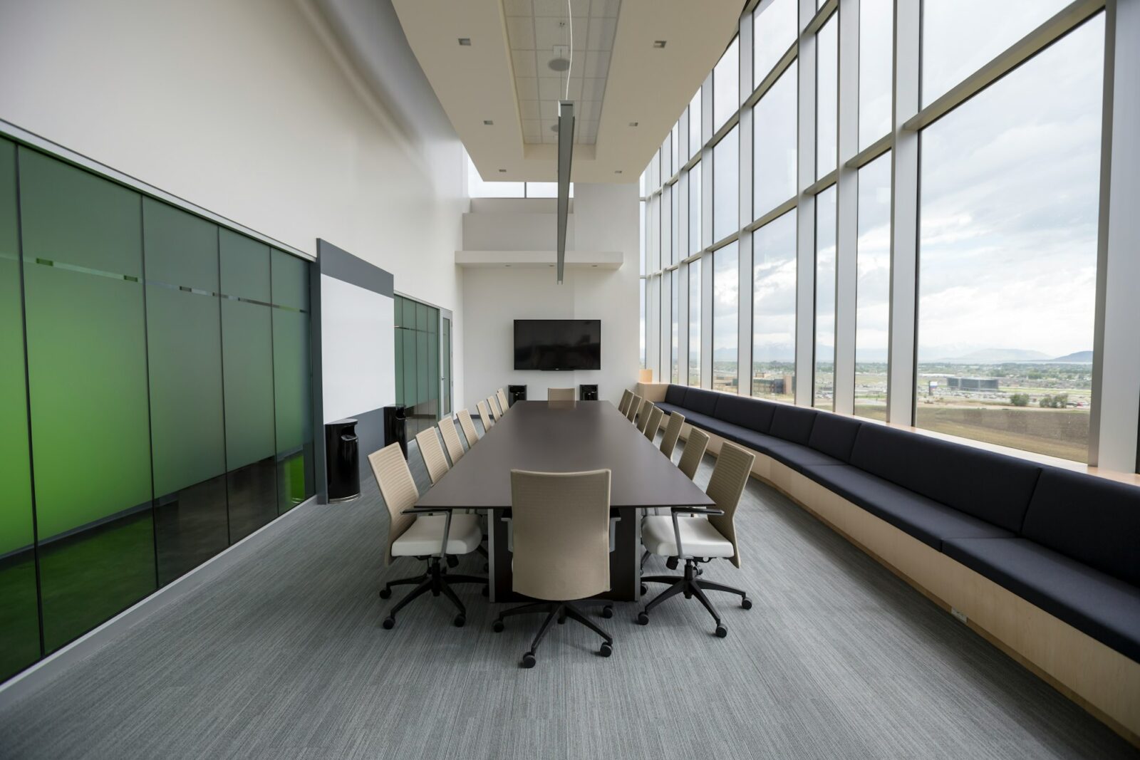 Empty boardroom with a long dark table, grey chairs and tall windows along one wall