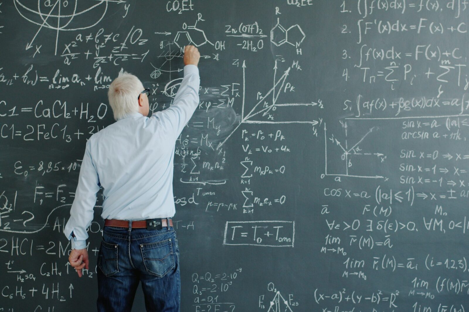 A teacher writing and underlining formulas in chalk on a classroom blackboard