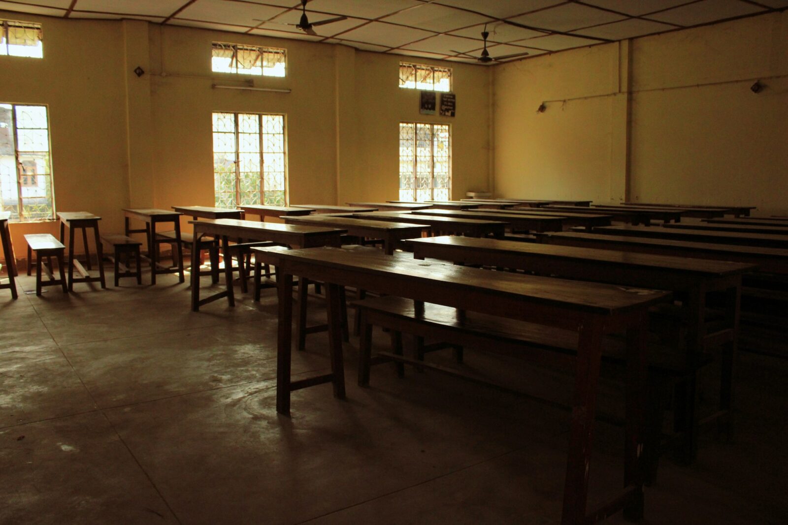 Empty college classroom with rows of wooden desks and benches under ceiling fans