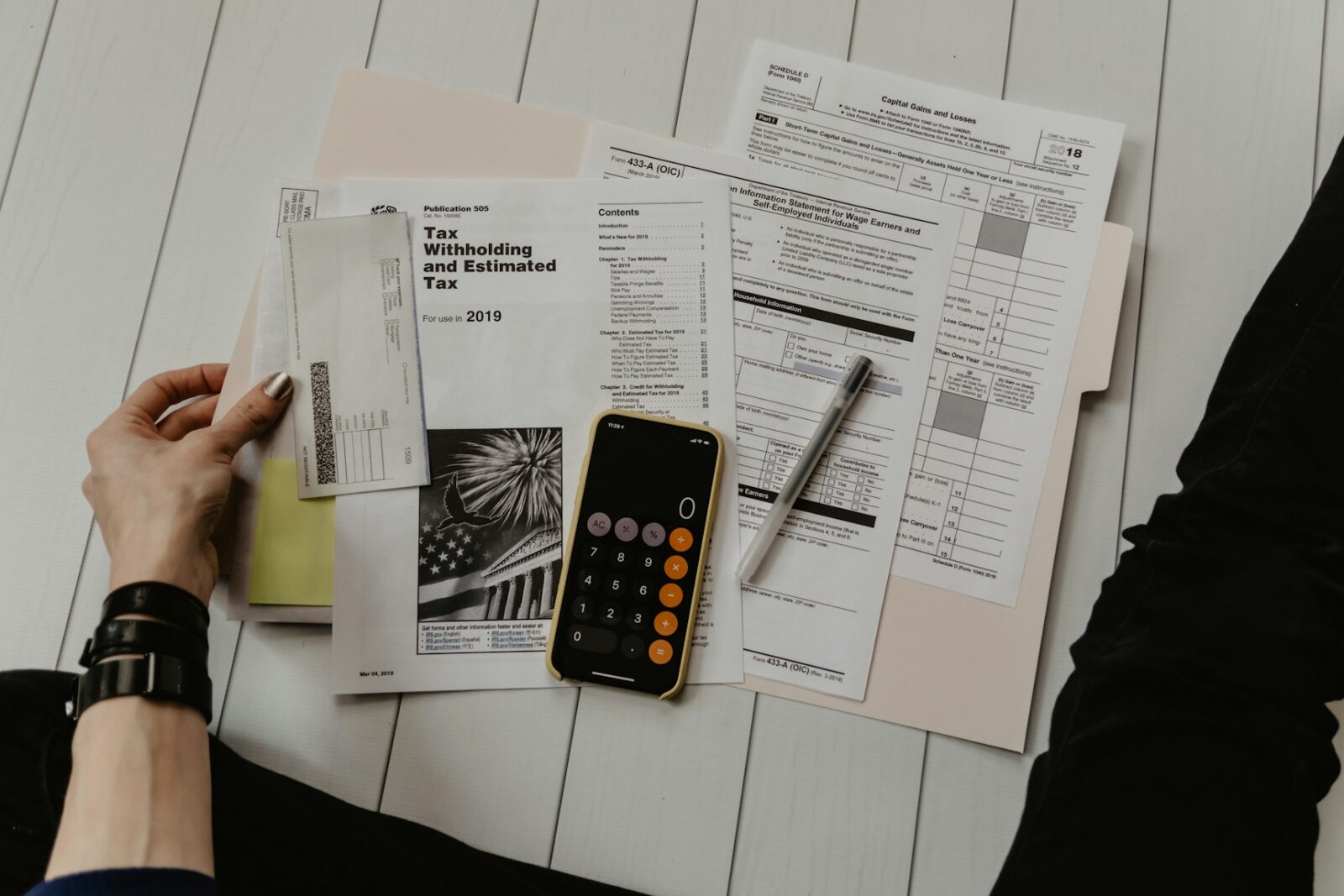 A person holding a sheet of paper beside a pen and a calculator