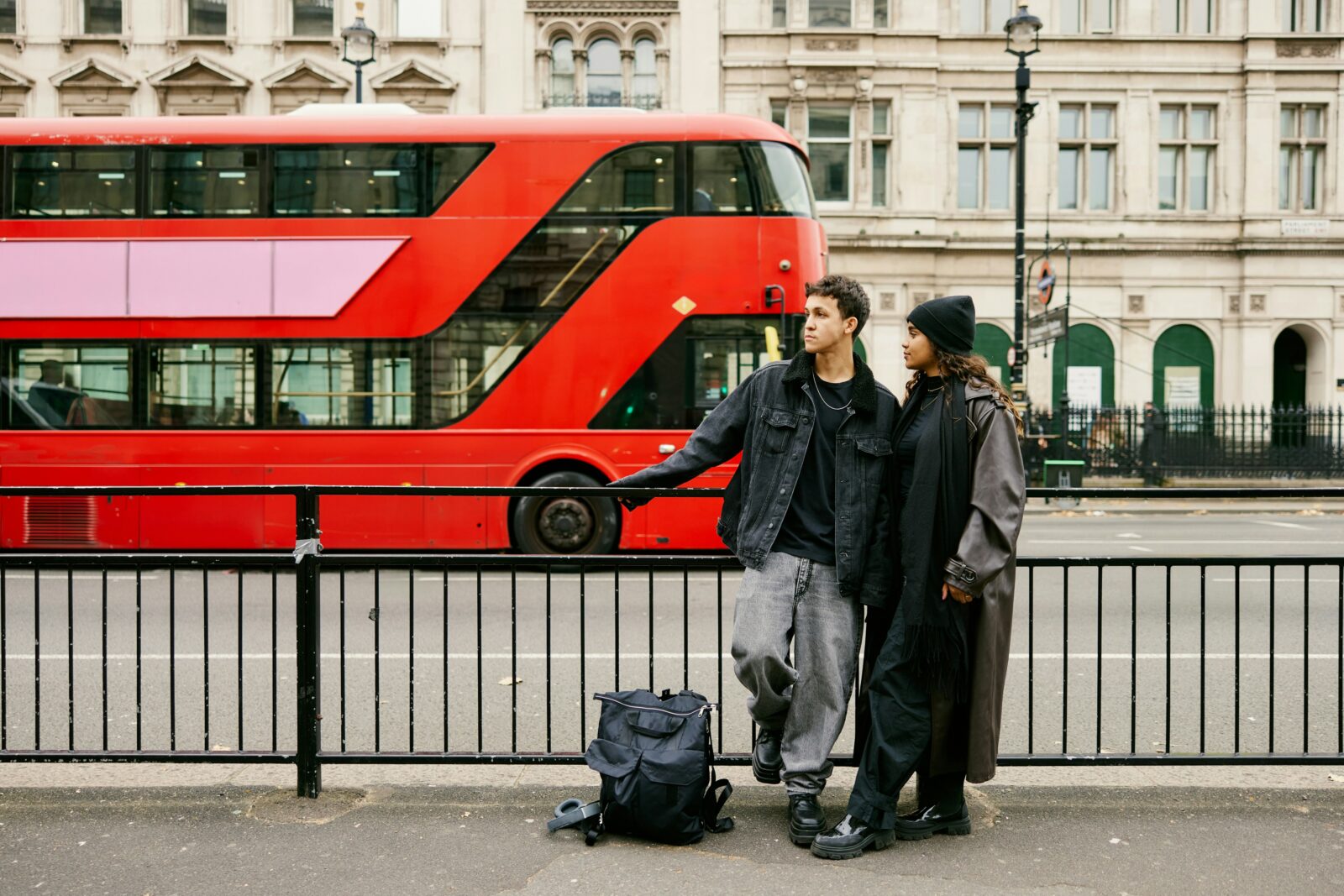 A young man and woman standing in front of a red double decker bus on a city street