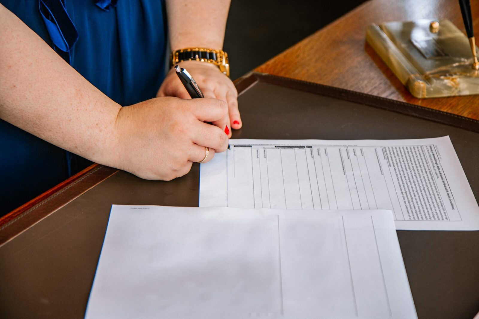 A person holding a pen and writing on paper at a table