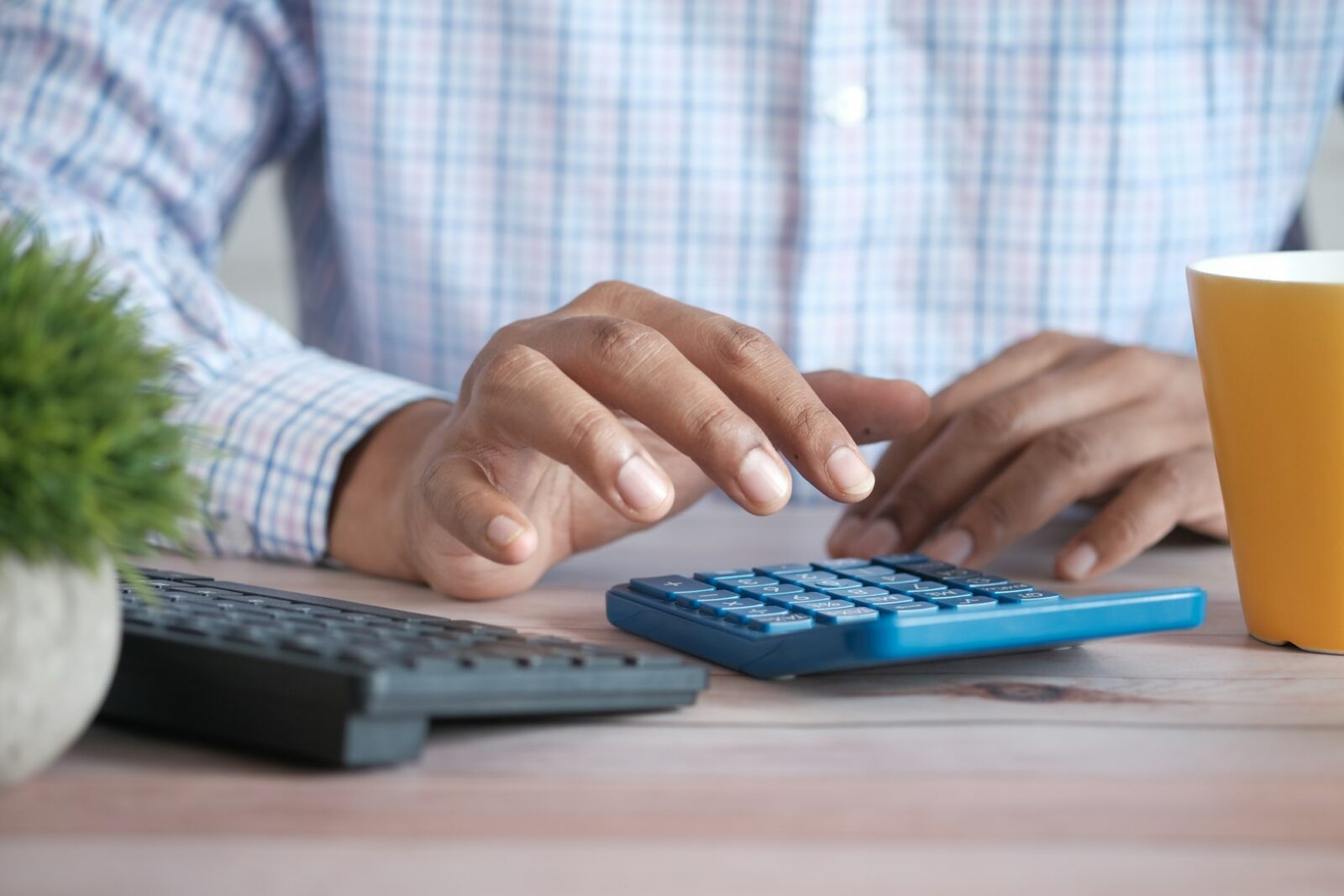 Close-up of a hand using a calculator on a desk beside a coffee mug