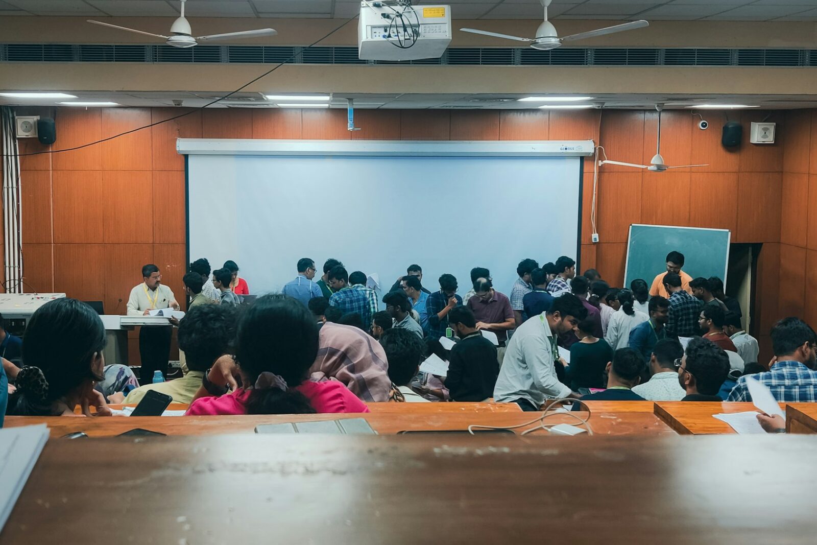 Students seated at long desks in a classroom, facing a projector screen