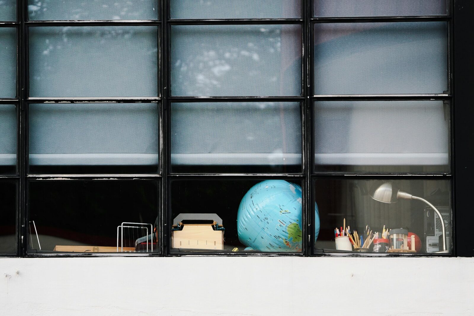 A study desk by a window with a globe, a lamp and stationery