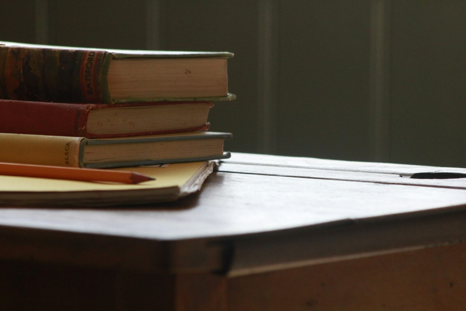 Old books and a pencil resting on a worn wooden school desk