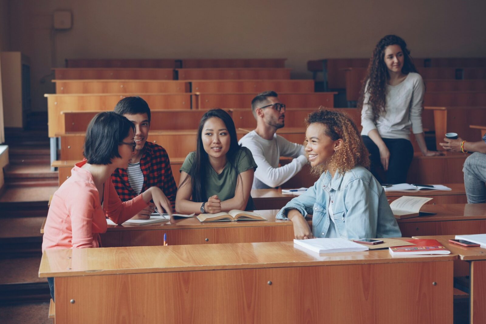 University students talking and studying at wooden desks in a lecture hall