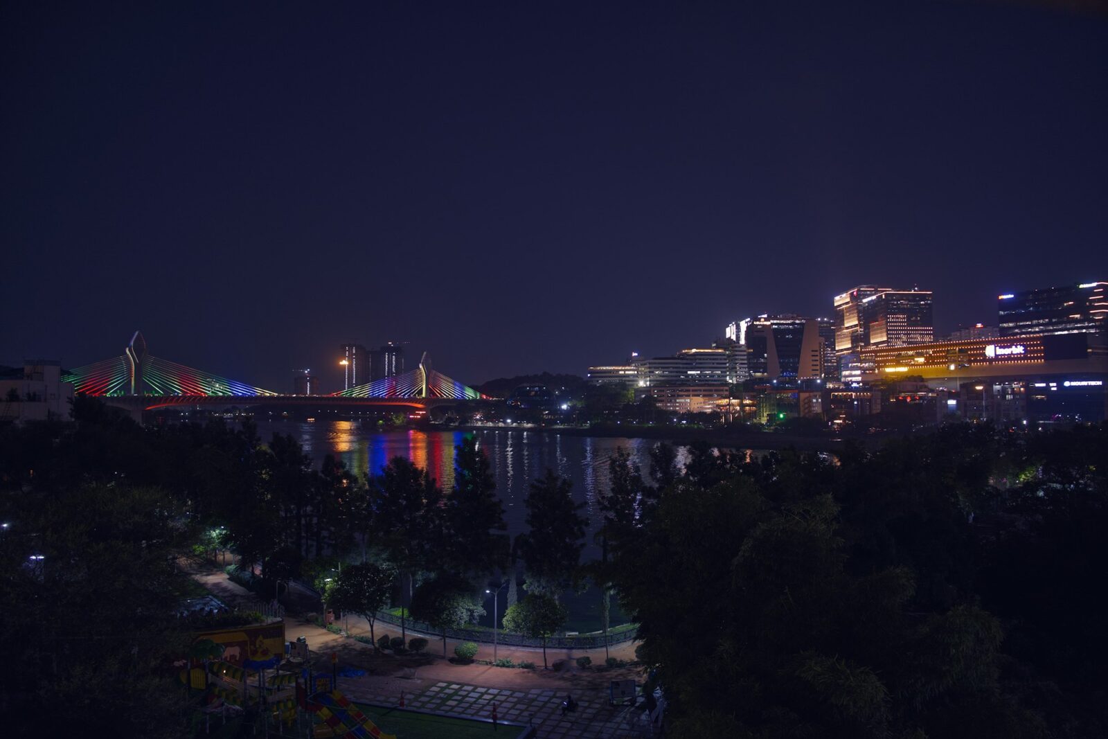 A city at night with a brightly lit bridge and colourful reflections on the water