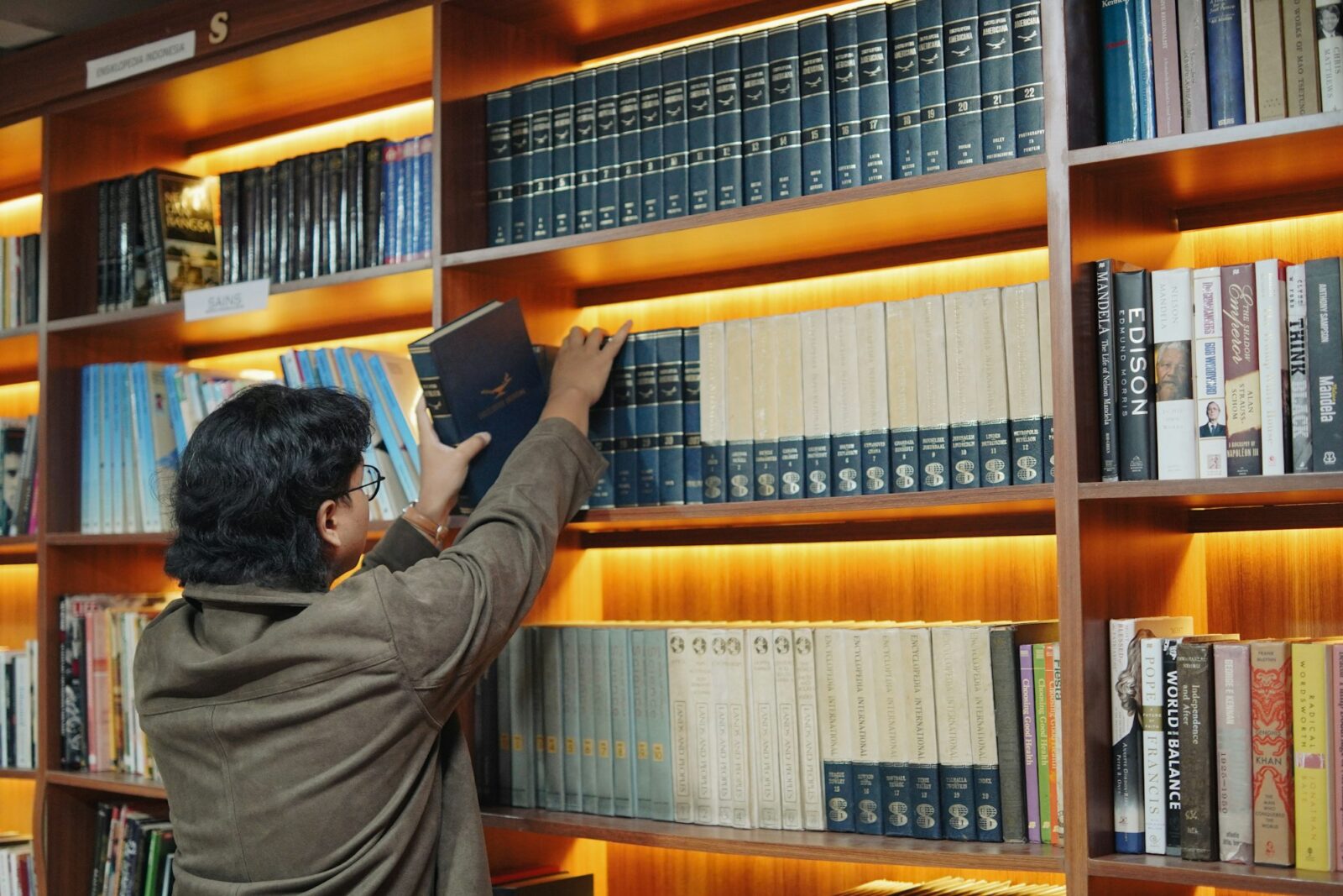 Person taking a book from a well lit wooden bookshelf in a library