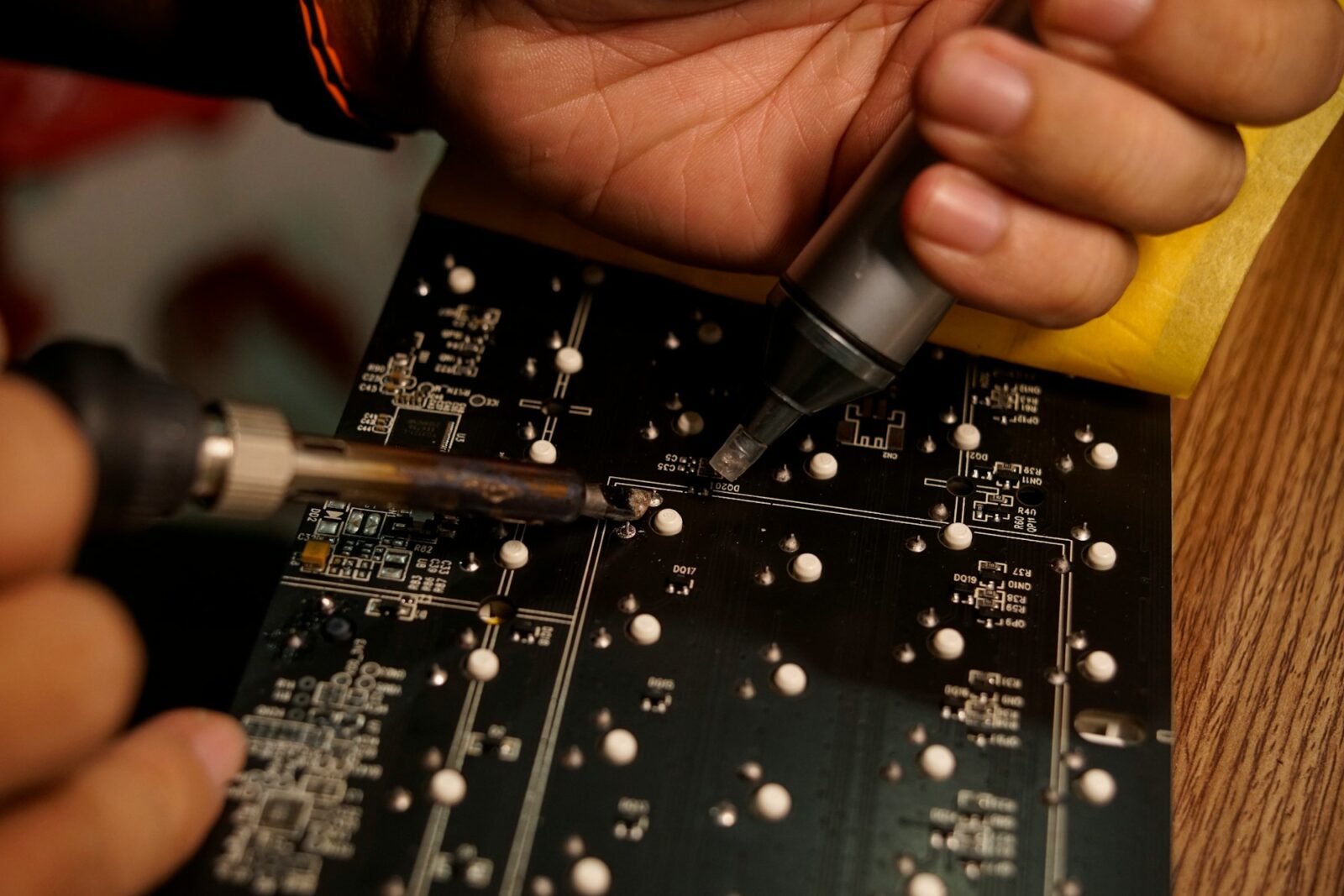 Sri Shakhti Institute of Technology, Coimbatore, students make a satellite for ISRO Hands using a soldering iron and a solder pump on a black printed circuit board