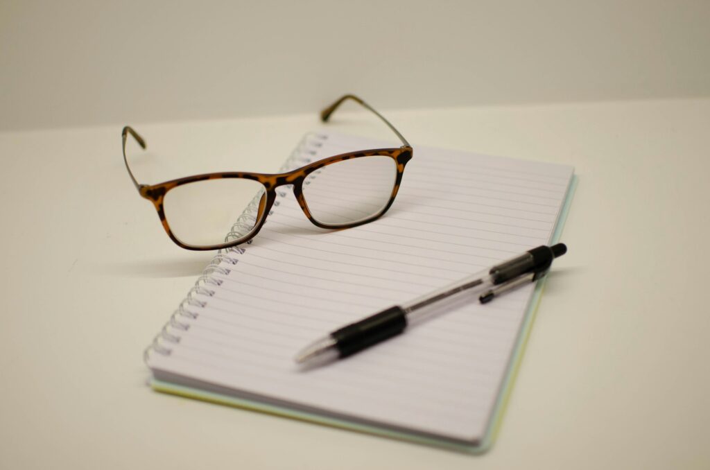 A pair of glasses and a pen resting on a blank spiral notebook