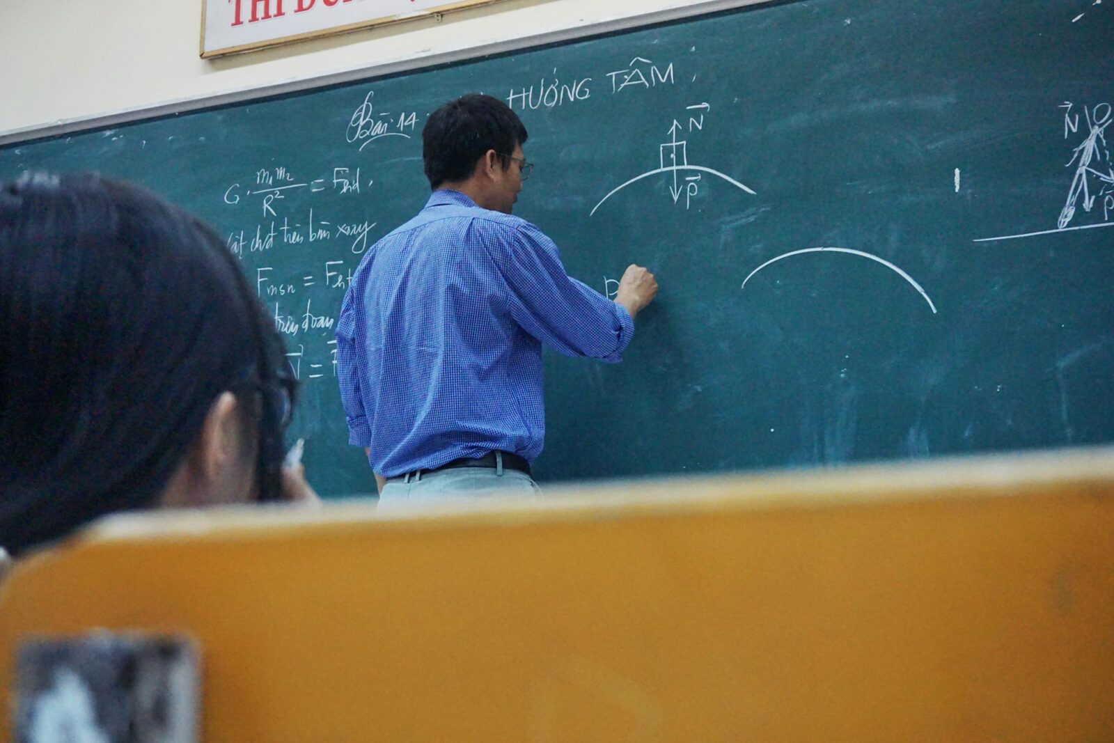 Are Teachers Paid Enough? A teacher writing physics equations on a green chalkboard in a classroom