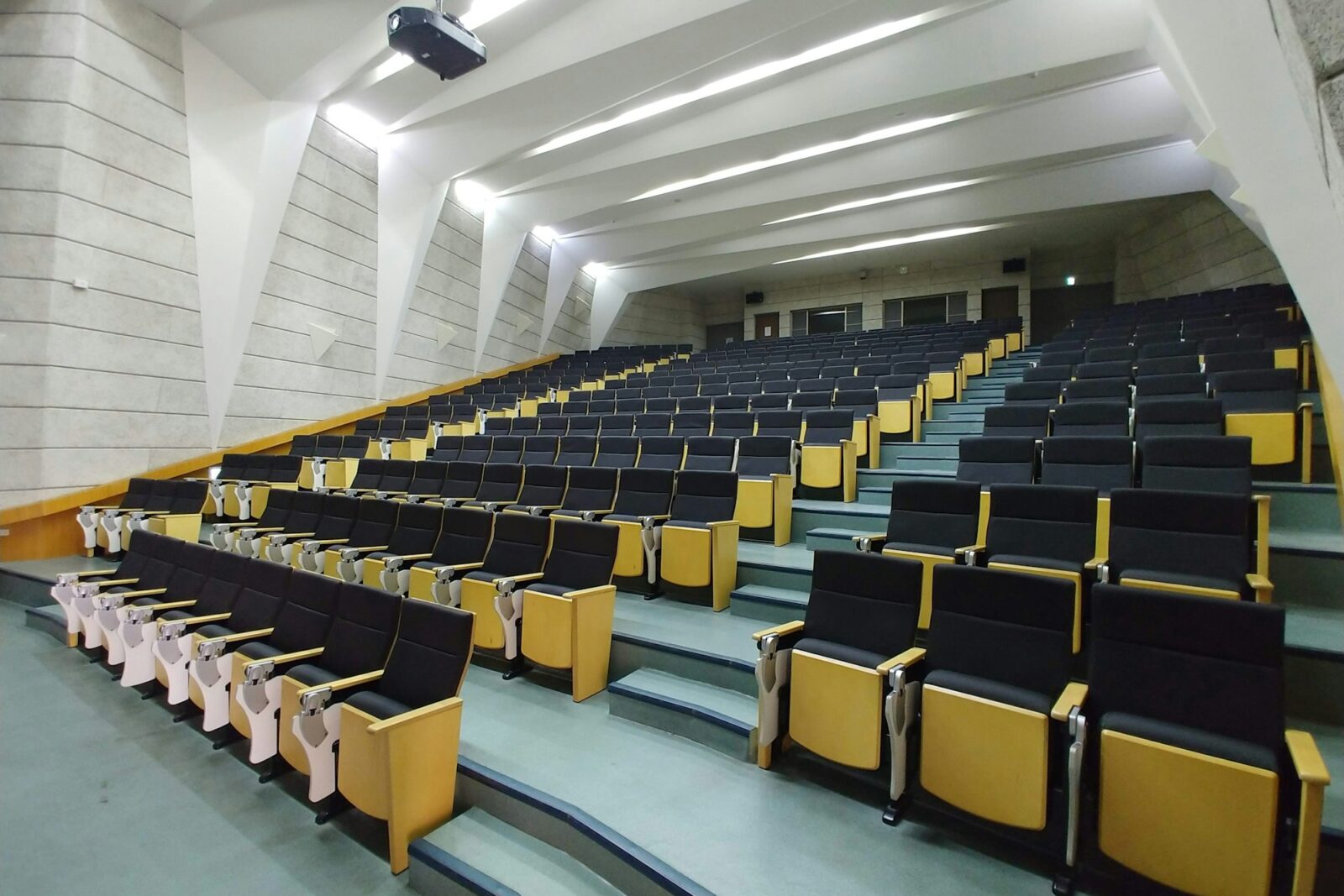 ‘Smart Class! A Way To A Smart Education Empty tiered lecture hall with rows of black and yellow seats and a projector fixed to the ceiling
