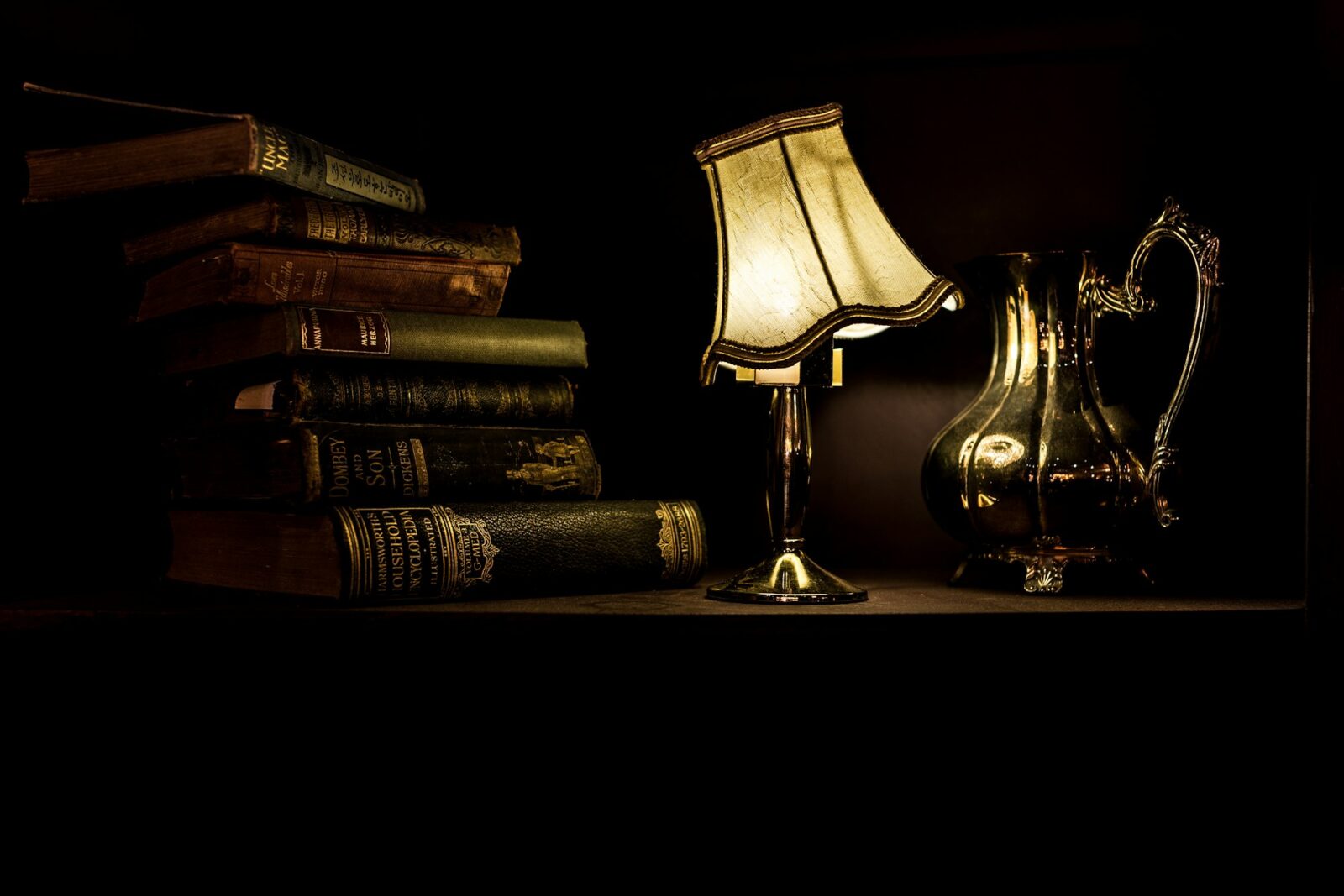 A vintage desk lamp glowing beside a pile of old books in a dark room