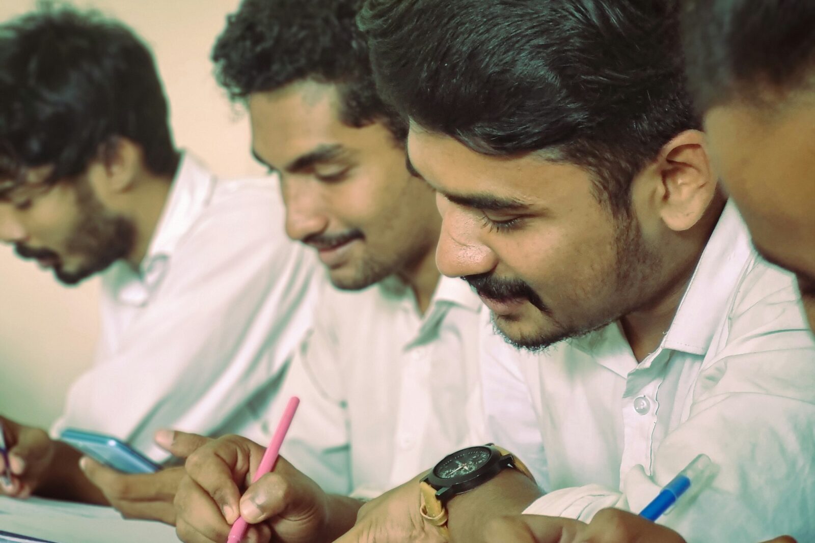 A group of young men writing notes at a table during a class