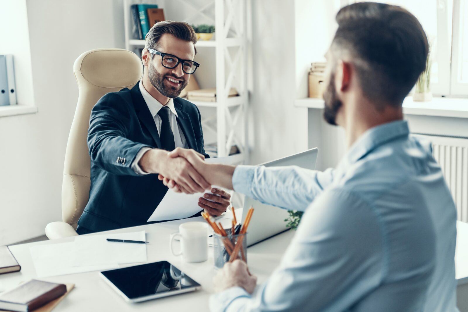 The Emerging Field Of HRM Smiling man in a suit shaking hands with a candidate across an office desk