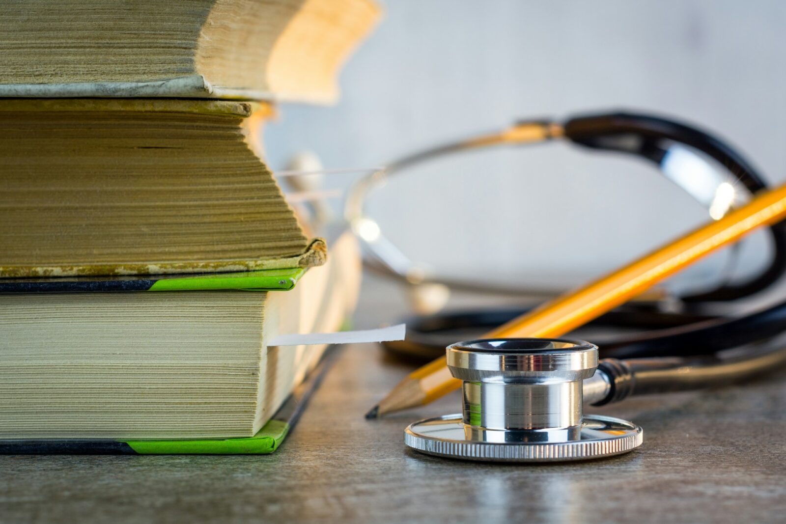A stethoscope resting on a pile of medical textbooks with bookmarks