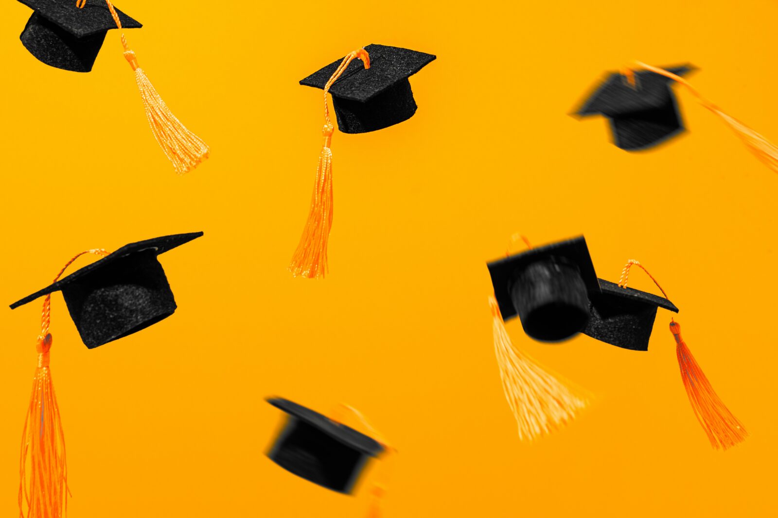 Top 9 Universities Offering Free Online courses Black graduation caps with orange tassels flying against a bright orange background