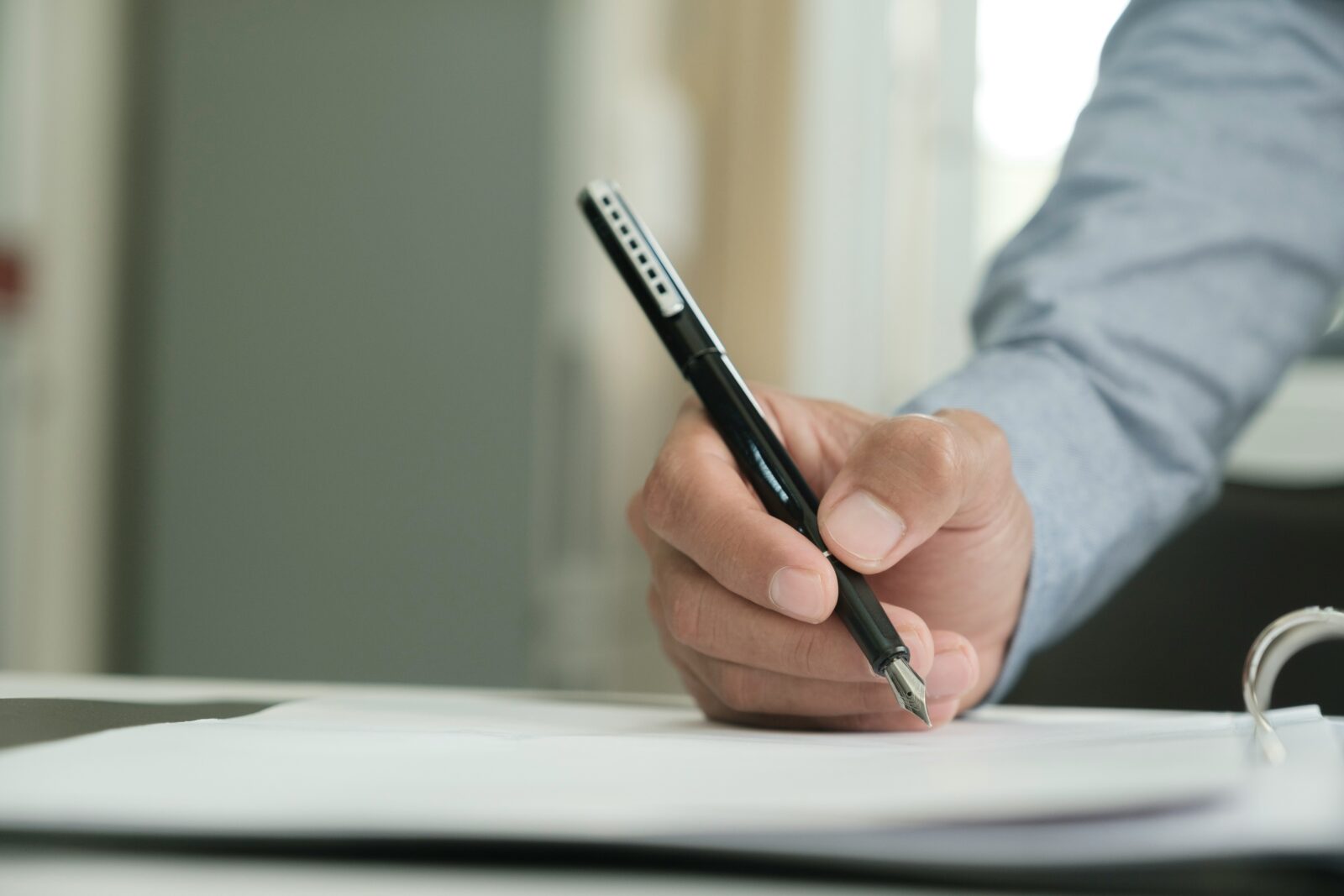 Close view of a hand signing papers in a ring binder with a black fountain pen