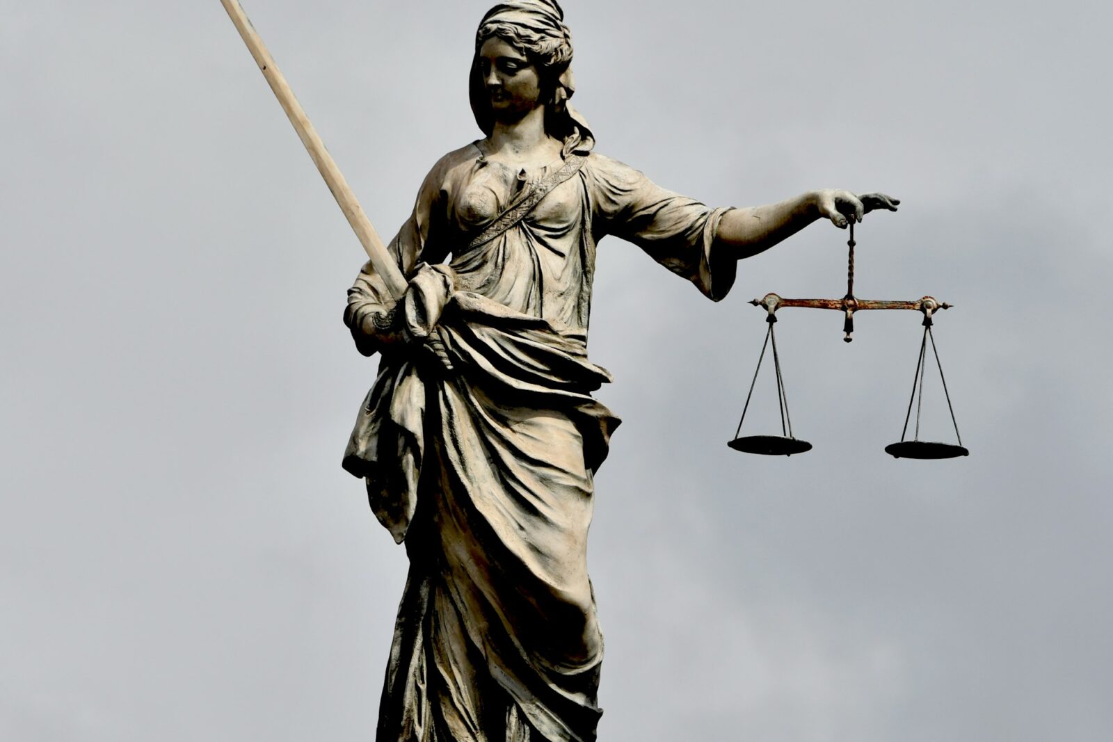 Statue of Lady Justice with sword and scales seen against a grey sky