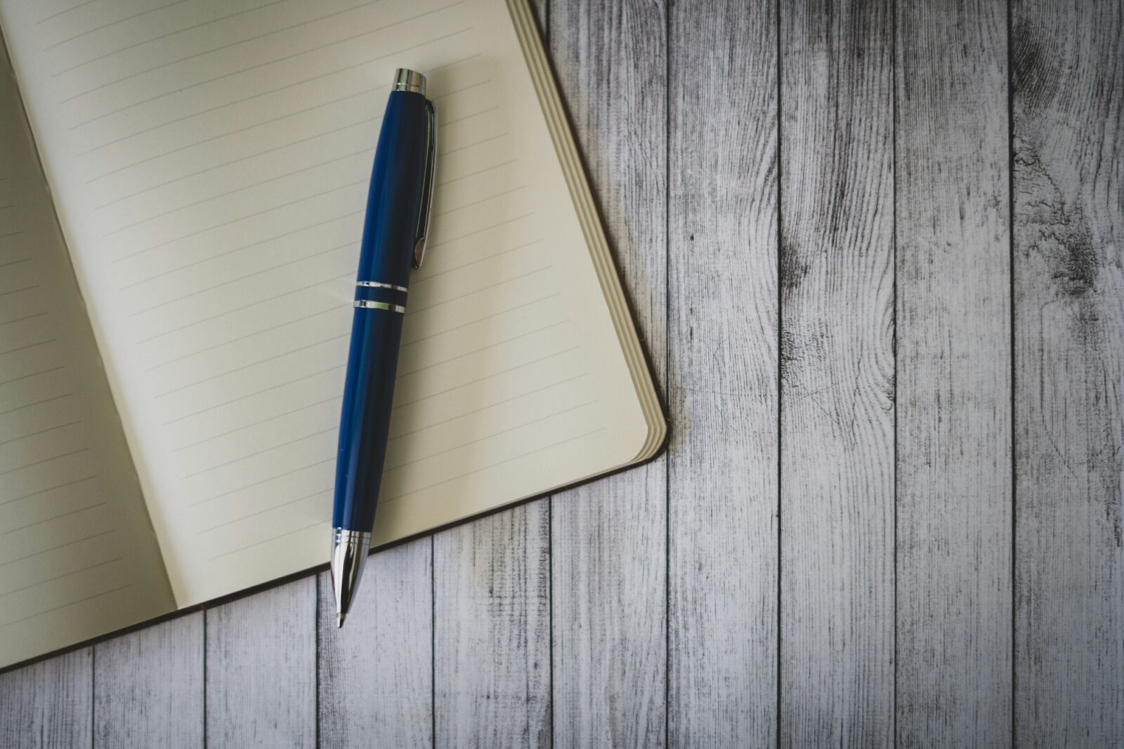 Blue ballpoint pen resting on an open blank notebook on a wooden table