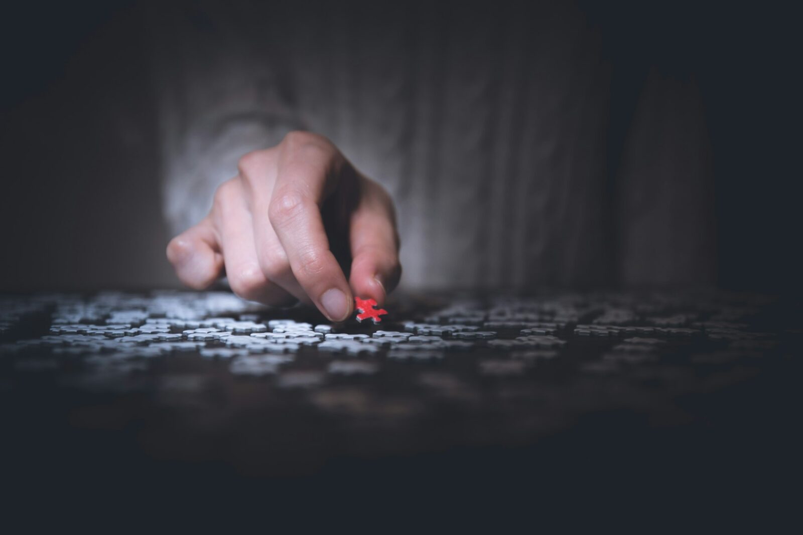 Hand holding a red jigsaw puzzle piece against a dark background