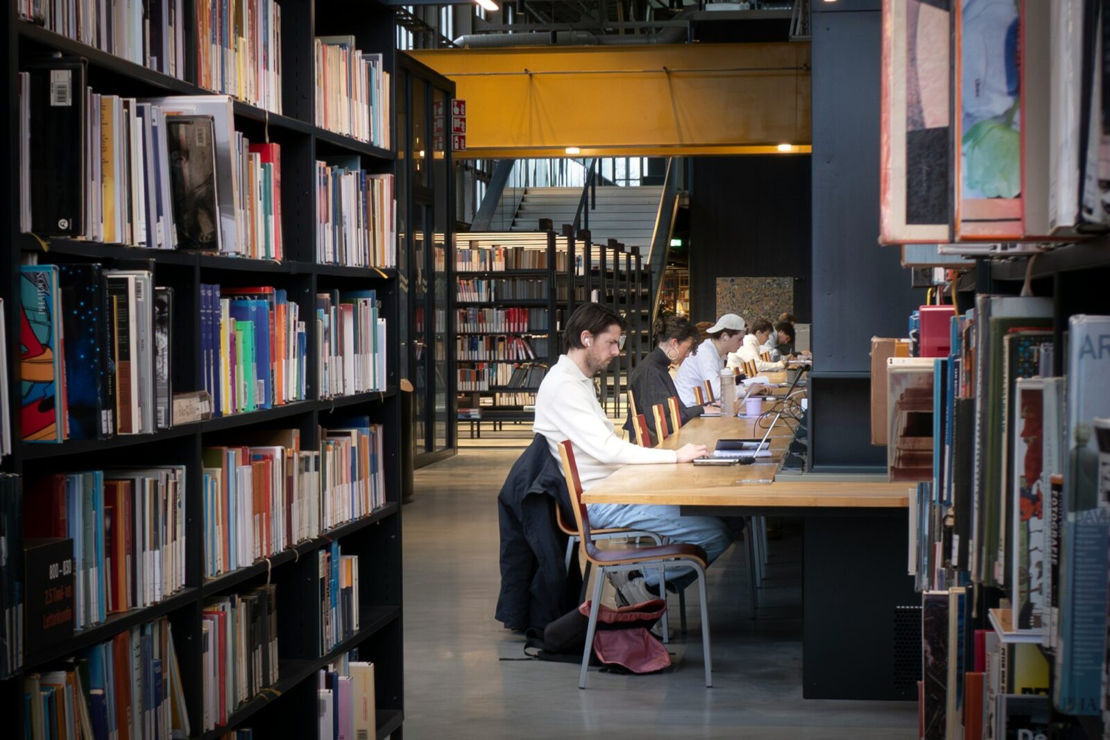 5 Tips For Studying Smarter In College Students studying quietly at long wooden tables in a modern library lined with bookshelves