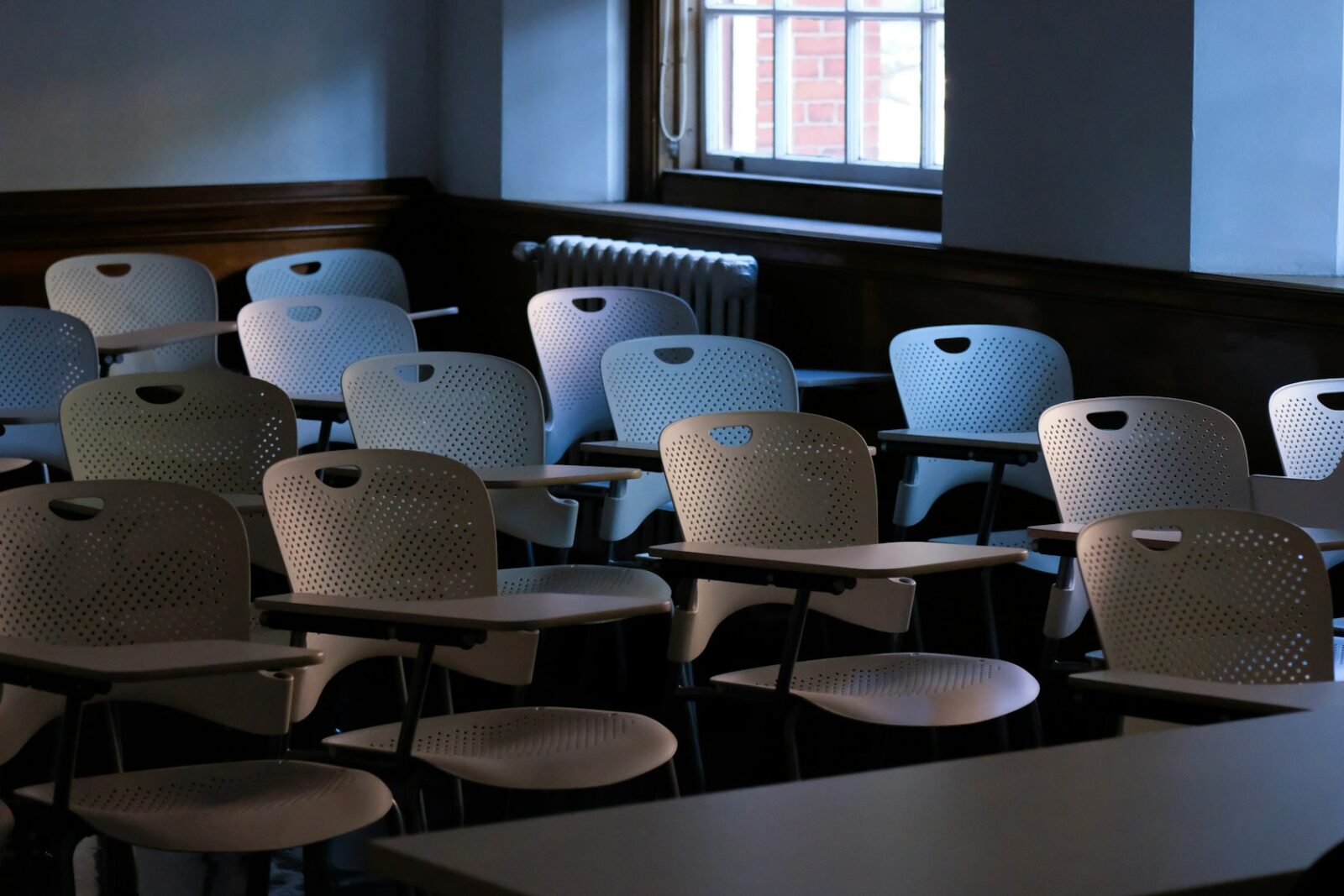 The impact of the pandemic on education and edtech Rows of empty white chairs with attached desks in a dim classroom