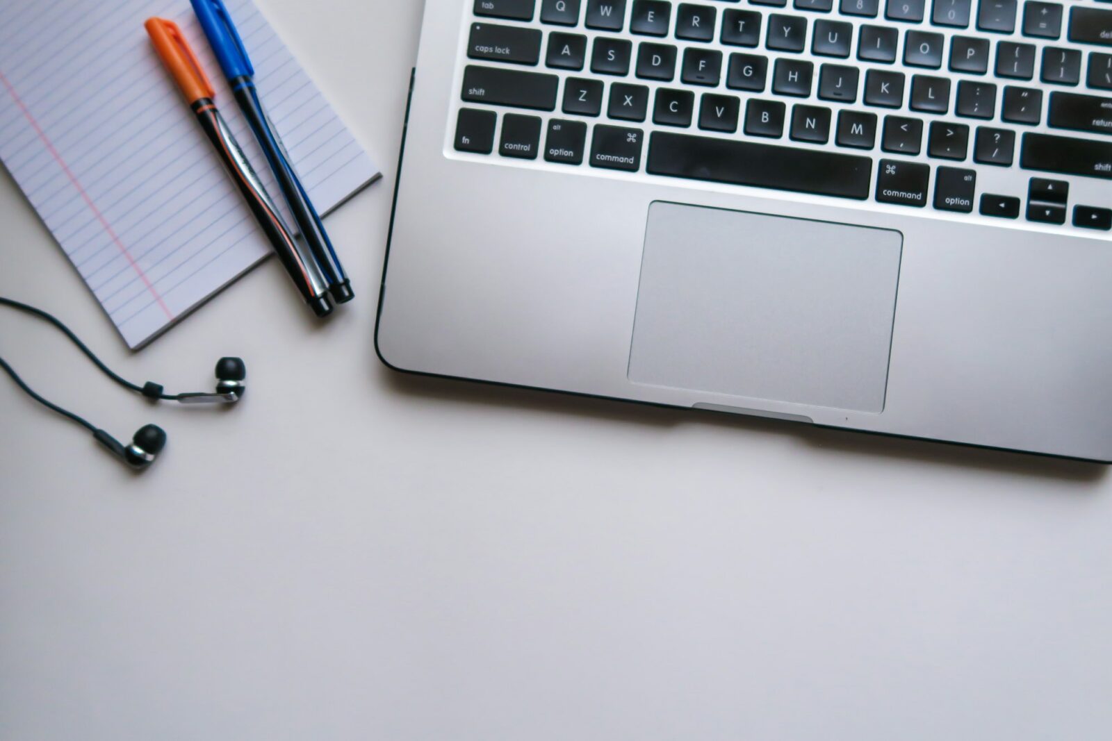 Top 10 Free Online Schools Silver laptop beside a sheet of ruled paper on a desk set up for remote study
