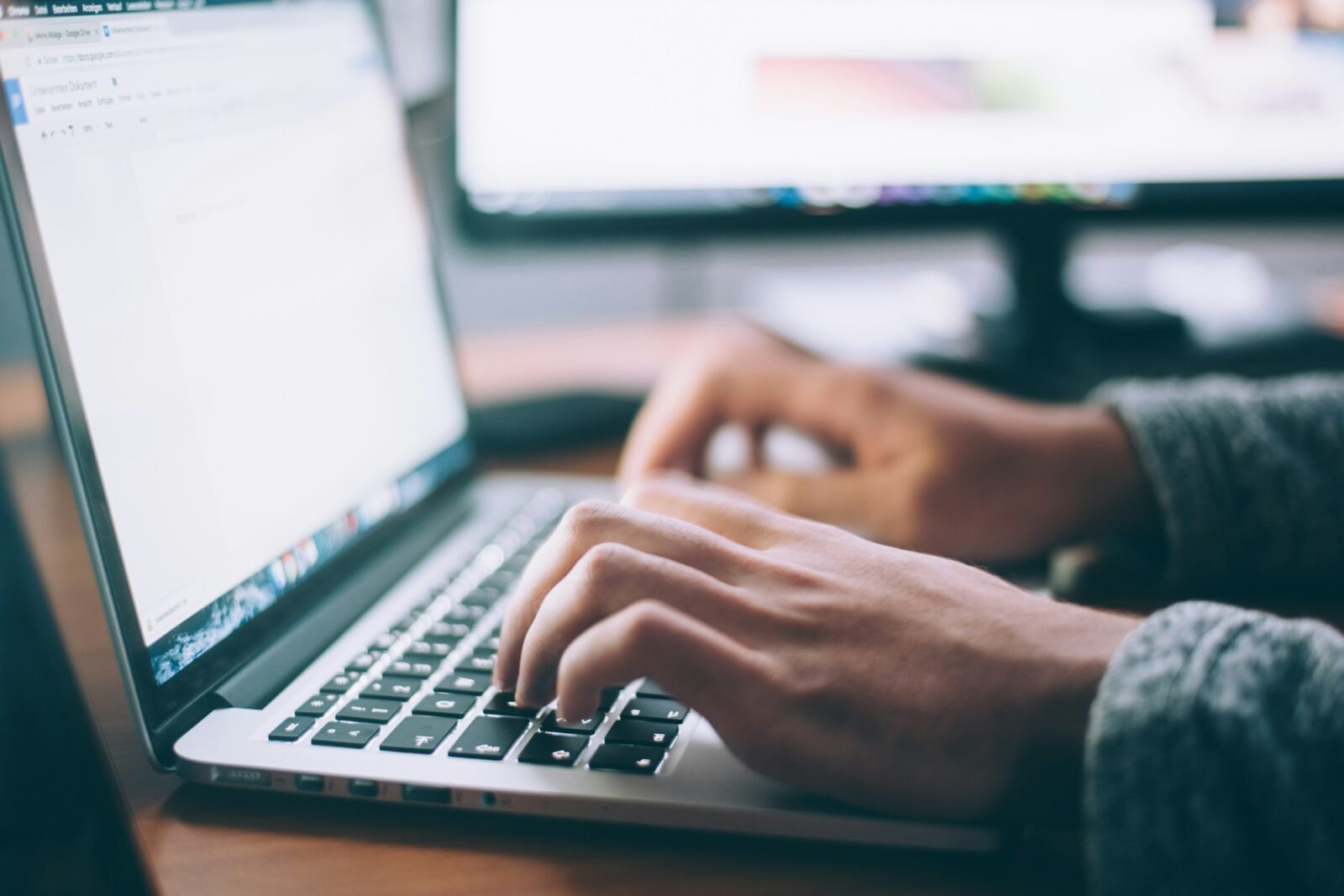 Person typing on a laptop keyboard at a bright white desk