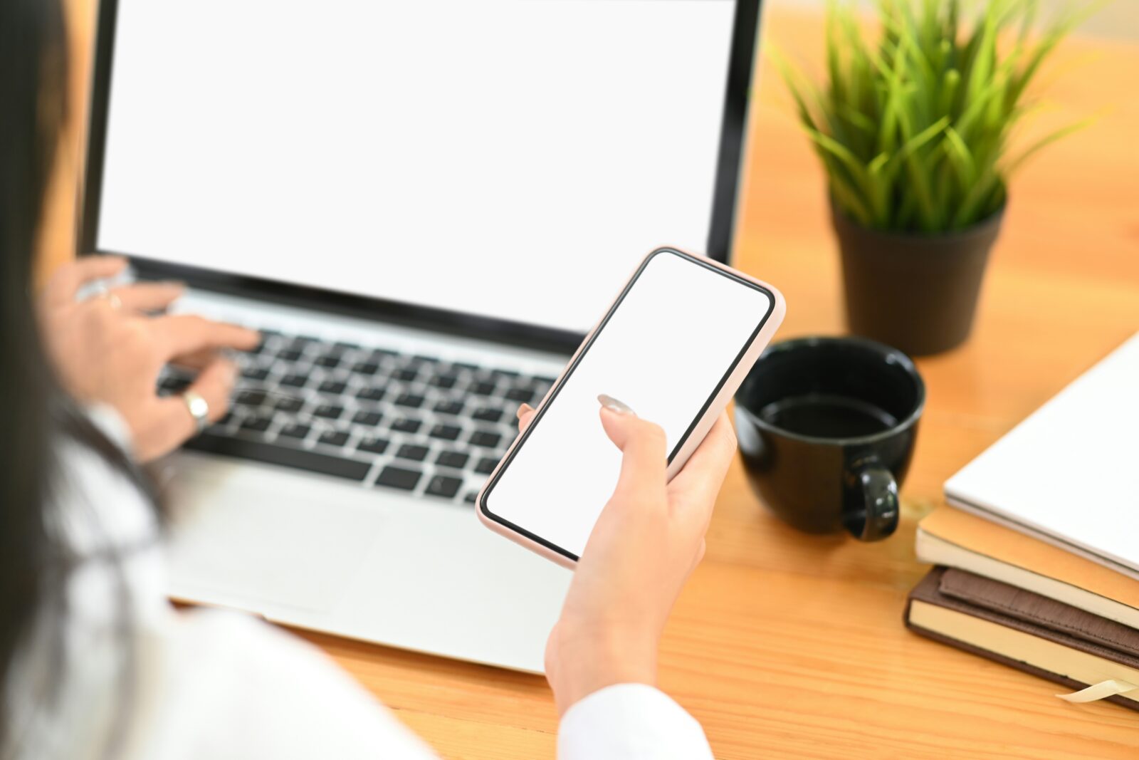 Cropped view of a woman working with a mobile phone and a laptop at a desk