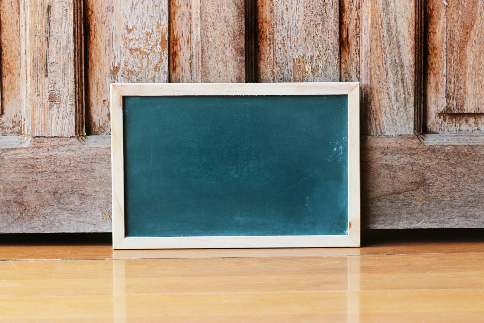 A small blank chalkboard in a pale wooden frame leaning against an old weathered wooden door