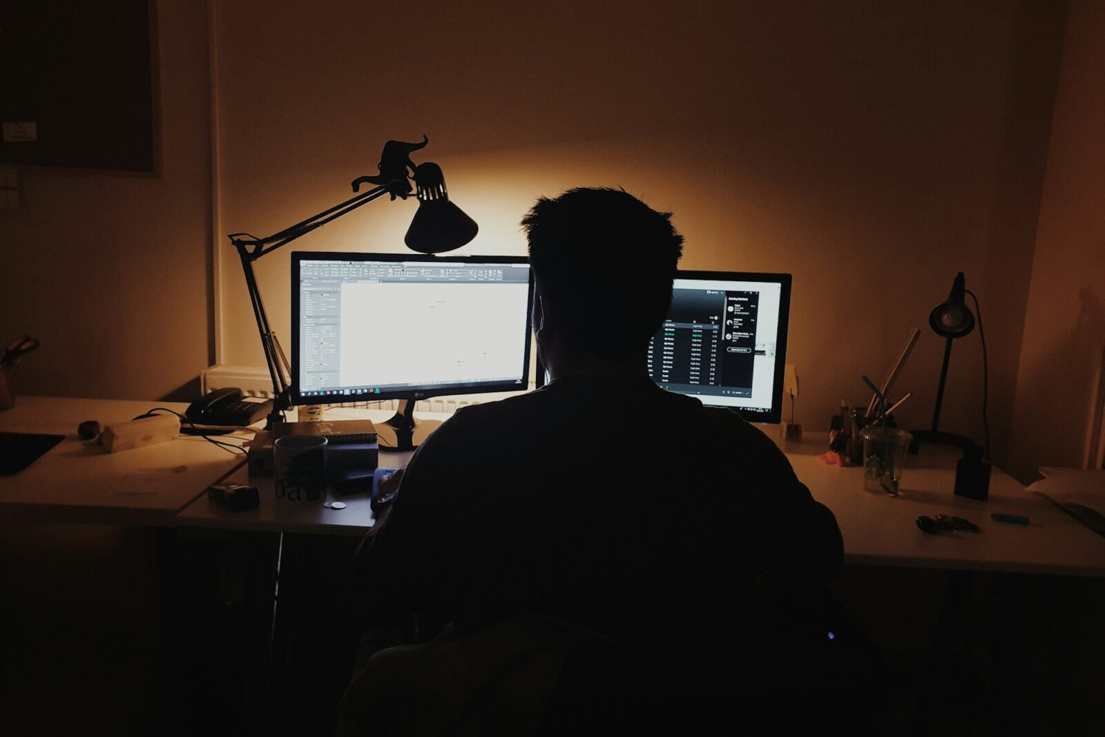 Person working alone at a desktop computer in a dimly lit room