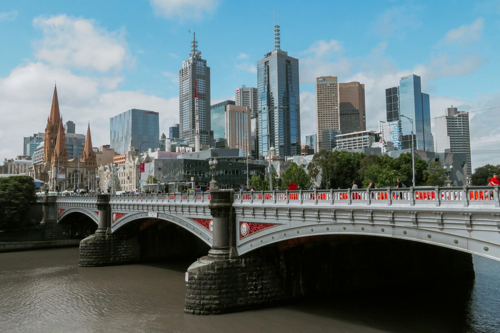 White footbridge over a river with the Melbourne city skyline behind on a clear day