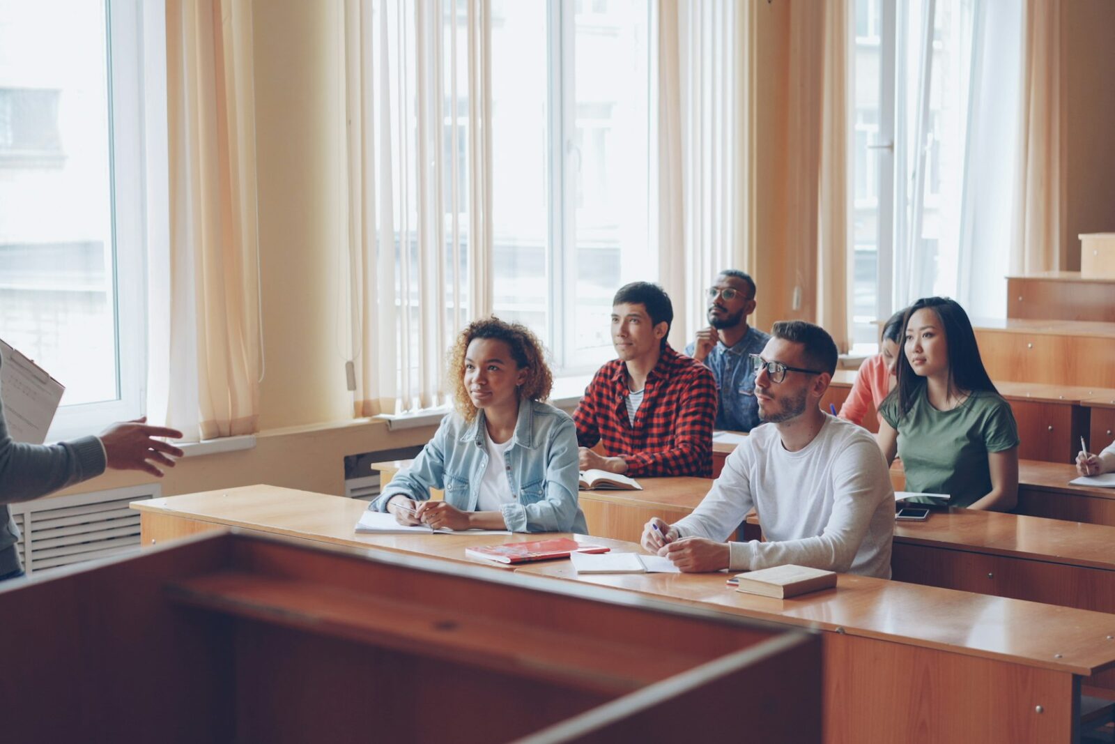 A teacher talks with smiling students seated at desks in a bright classroom