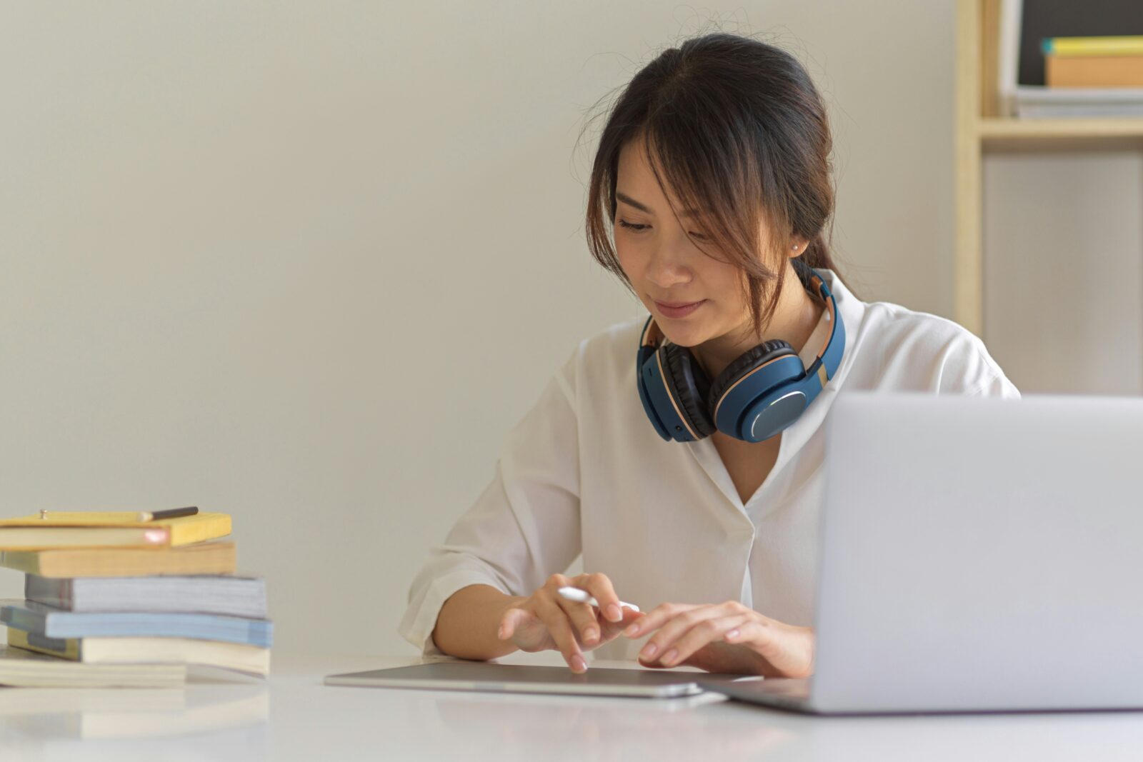 How Artificial Intelligence in best Online Learning Revolutionising A woman with headphones round her neck uses a stylus on a tablet beside a laptop and a stack of books
